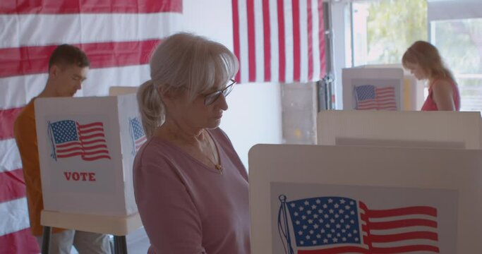 A group of diverse and focused voters voting at a polling station with sliding glass doors, American flags and trees in the background