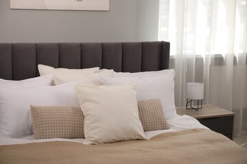 Many soft white pillows and blanket on bed indoors