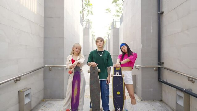 Portrait group of Young Asian man and woman friends skating on longboard skate at public park on summer vacation. Stylish people have fun urban lifestyle outdoor sport skateboarding at city street.
