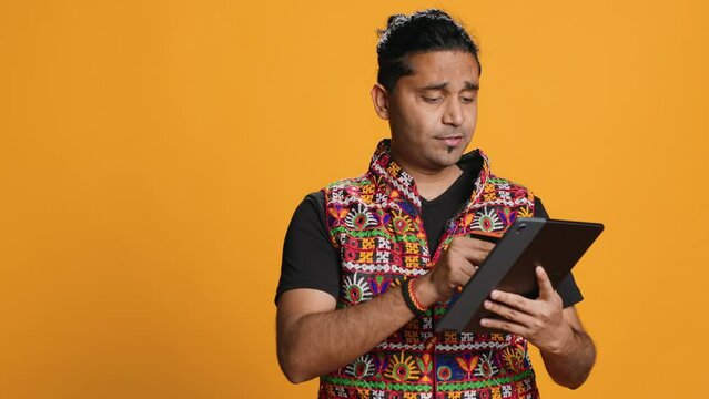 Man adding payment method on shopping website using tablet, taking advantage of promotions, studio background. Indian person buying stuff online using credit card, typing data on device, camera A