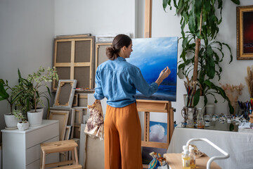 Professional female artist working on picture. Back view, woman concentratedly thoughtfully...
