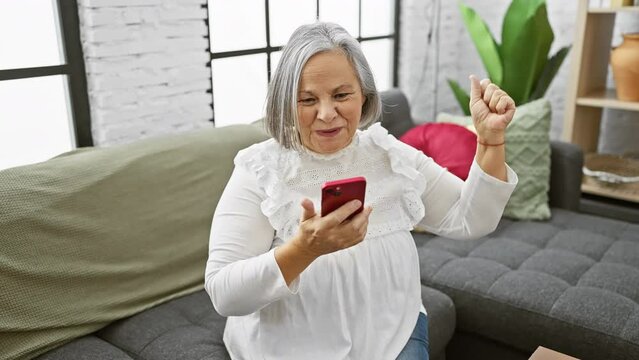 A mature woman interacts with her smartphone expressing surprise in a cozy living room setting