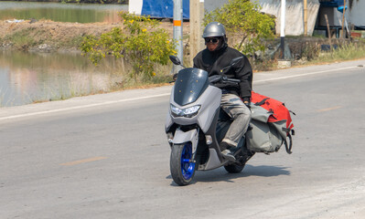 Naklejka premium Motorcyclist rides with delivery in the large bags, Thailand.