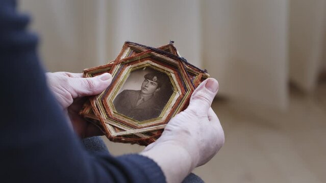 A senior woman cradles an old framed photo of a soldier, capturing a moment of reflection and remembrance.