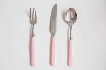a pink fork  knife and spoon on a white surface