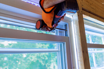 In new house, construction worker installs plastic windows using screwdriver