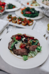 Fresh salad with beef, tomatoes, green leaves on white tablecloth