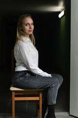 Portrait of a young beautiful blonde girl in a white shirt on a dark background.