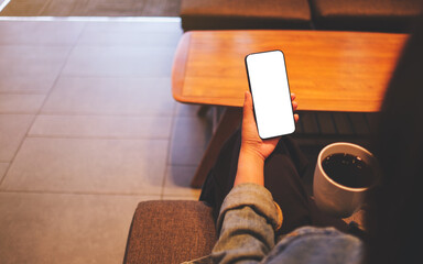 Mockup image of a woman holding mobile phone with blank desktop screen while drinking coffee in cafe