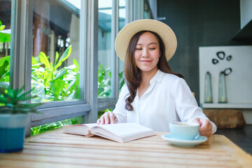 Portrait image of a beautiful young woman with hat drinking coffee while reading book