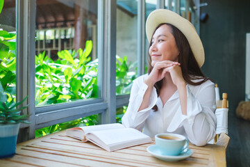 Portrait image of a beautiful young woman with hat while reading book and drinking coffee