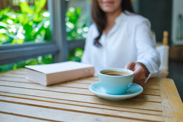 Closeup image of a woman drinking coffee with a book on table