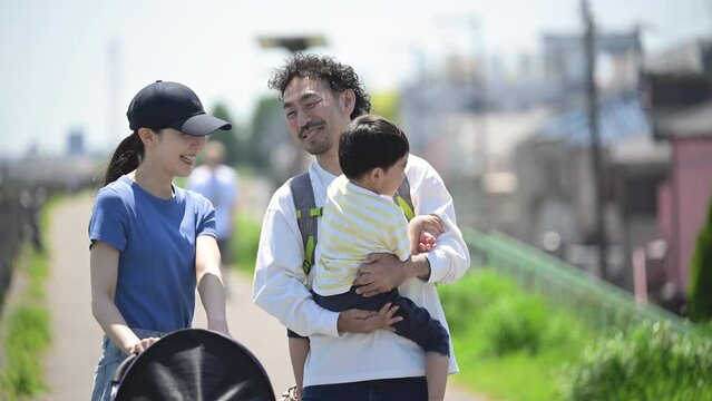 晴天の川沿いの公園で散歩する親子(3人家族)の上半身　春夏のお出かけやレジャーなどのイメージ　笑顔で大笑いで見上げるスロー動画