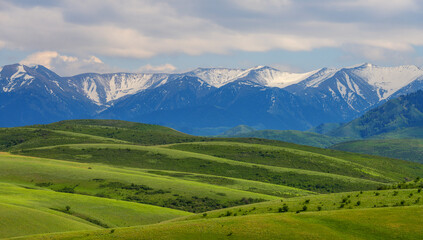 Fototapeta premium A picturesque hilly valley against the backdrop of the snow-covered mountains of the Dzhungar Alatau (Kazakhstan)