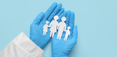 Doctor holding family figures on blue background. Health care concept