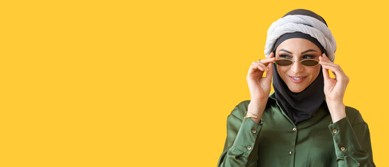 Stylish Muslim woman in sunglasses on yellow background, closeup