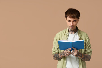 Young tattooed man reading book on brown background