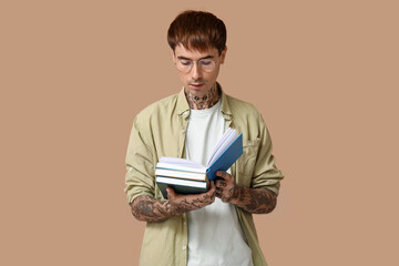 Young tattooed man with books reading on brown background