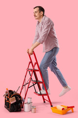 Young man with ladder and builder's tools on pink background