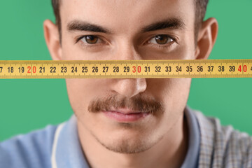 Young man with tape measure on green background, closeup