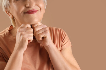 Mature woman doing face building exercise on beige background, closeup