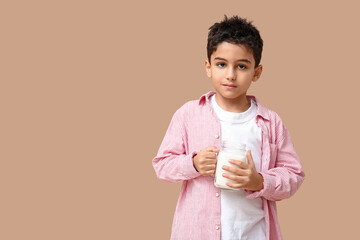 Cute little boy with mason jar of milk on beige background