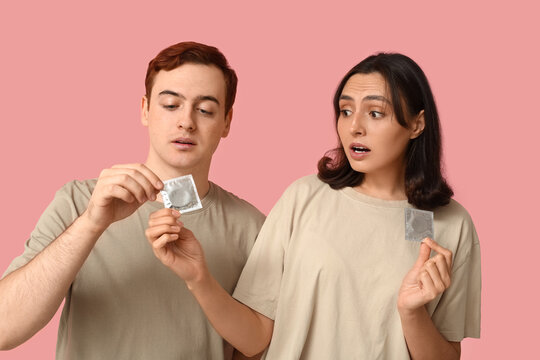 Young couple with condoms on pink background. Safe sex concept