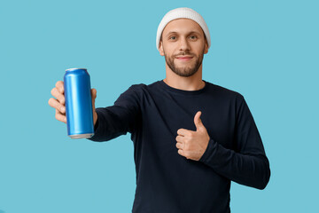 Young man holding can of cold beer and showing thumb-up gesture on blue background