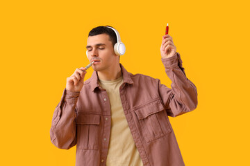 Young man with electronic cigarettes and headphones on yellow background