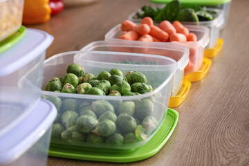 Plastic containers with vegetables for freezing on wooden table, closeup
