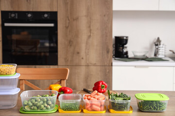 Plastic containers with vegetables for freezing on wooden table in kitchen