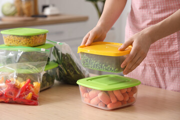 Woman stacking plastic containers with vegetables for freezing on wooden table