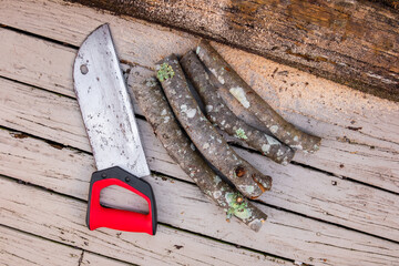 Old rusty handsaw over a wooden boards background with logs of cut firewood.
