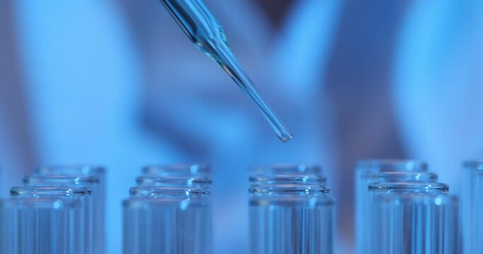 Chemist uses glass pipette dropping reagent into tubes