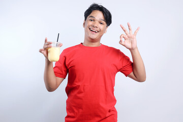 Cheerful Young Asian Guy Showing Ok Sign While Holding Juice Drinks And Isolated On White Background