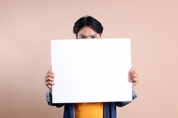 Potrait Of Young Asian Man Holding Placard And Peeking Isolated On Beige Background