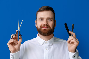 Young bearded man with open razor and scissors on blue background