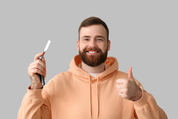 Young bearded man with open razor showing thumb-up on grey background