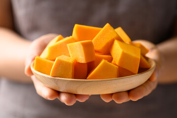 Chopped orange Hokkaido pumpkin on wooden plate holding by hand, Food ingredient