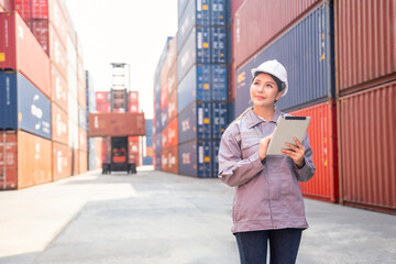 young asian woman standing at terminal port,using digital tablet inspect cargo container, a worker working in shipping yard,concept of cargo container transportation,logistics,business,industry