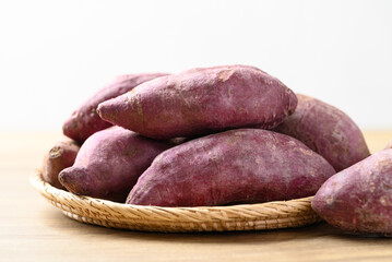 Raw purple sweet potatoes in basket on wooden table with white background, Food ingredient