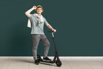 Young man with modern electric kick scooter near green wall