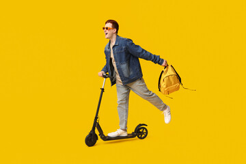 Male student riding modern electric kick scooter on yellow background