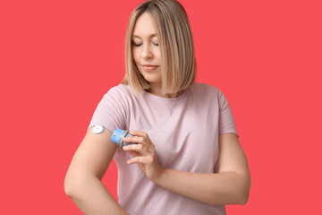 Woman with glucose sensor for measuring blood sugar level and applicator on red background....