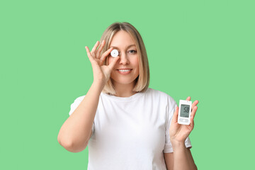 Woman with glucose sensor and glucometer on green background. Diabetes concept