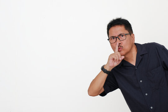 Adult Asian guy putting his fore finger in his lips gesturing to get some silence