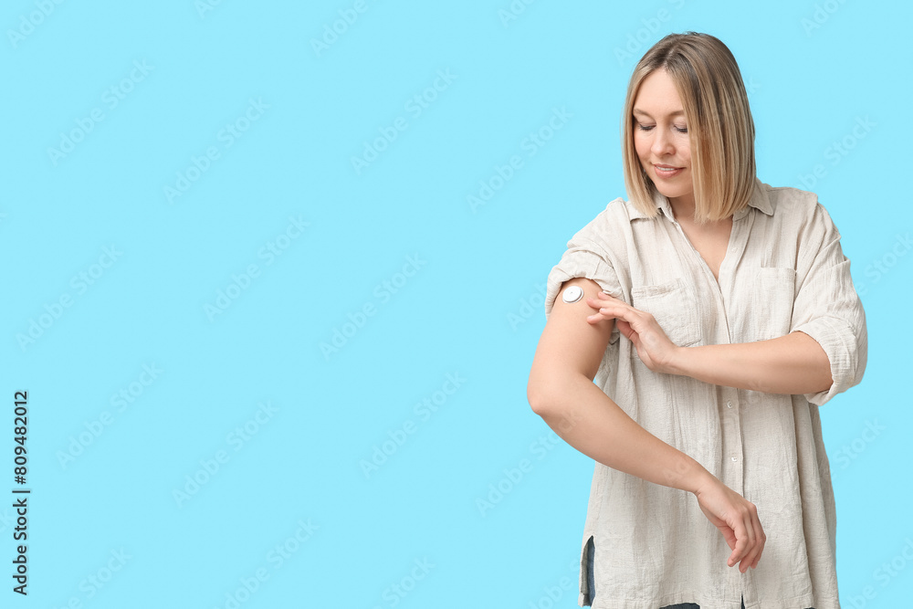 Wall mural woman with glucose sensor for measuring blood sugar level on blue background. diabetes concept