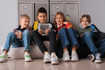 Little pupils using gadgets near locker at school