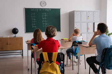 Little pupils sitting at desks and locker in classroom, back view