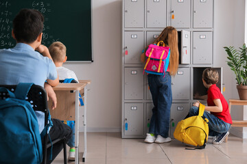 Little pupils near locker in classroom, back view